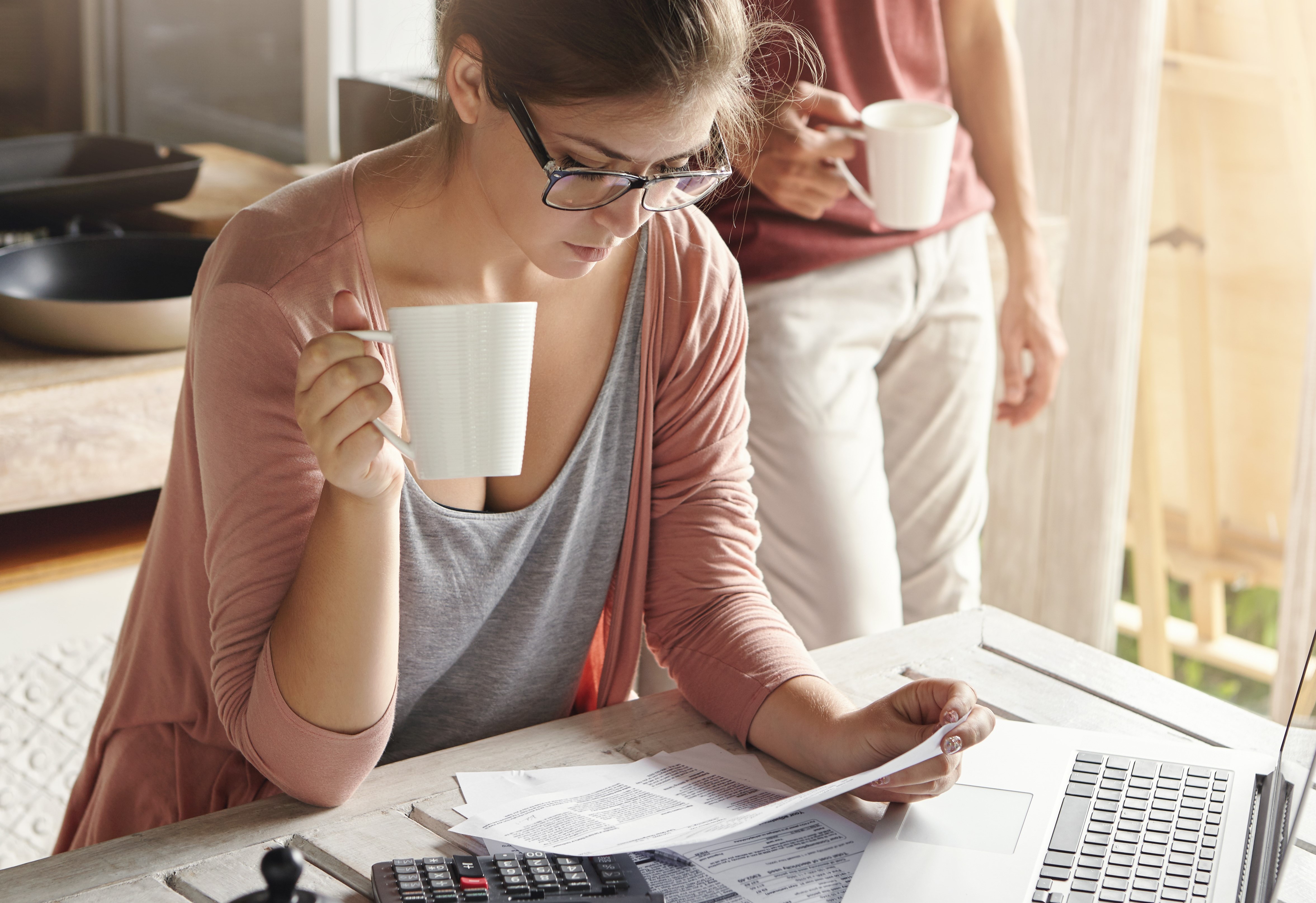 young-female-drinking-tea-studying-bill-her-hands-having-frustrated-look-while-managing-family-budget-doing-paperwork-sitting-kitchen-table-with-papers-calculator-laptop-computer.jpg?Revision=jzM&Timestamp=QxRKfk